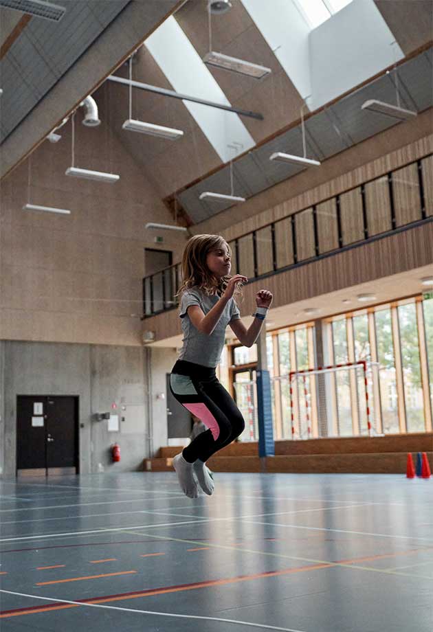 Jente som leker i gymsalen under VELUX overlysmoduler – Nordlys