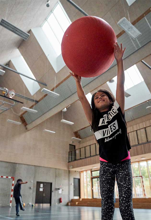 Dziewczynka gra na sali gimnastycznej pod systemem doświetleń modułowych VELUX — pasmo świetlne szedowe Northlight